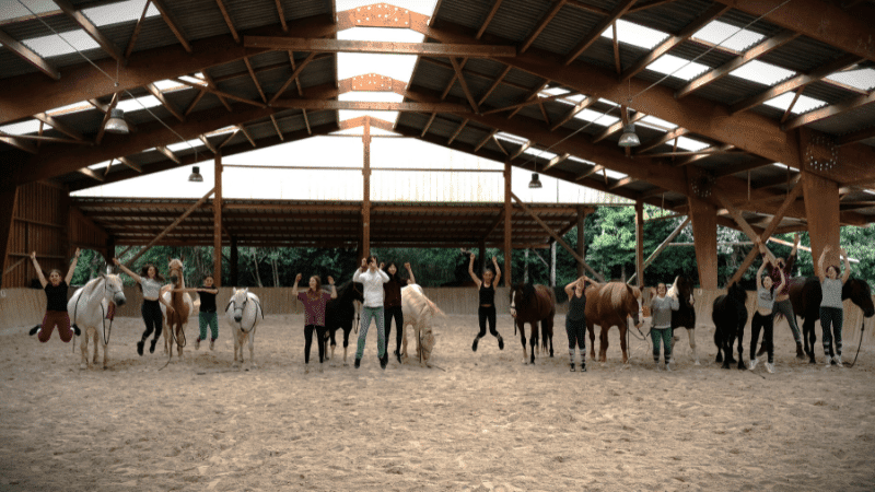 Adolescents et chevaux alignés dans le manège couvert des Crinières de l'Ouest.