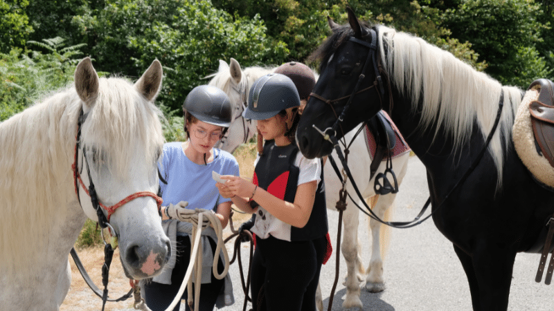 Deux cavalières vérifient une carte avec leurs chevaux lors d'un parcours d'orientation.