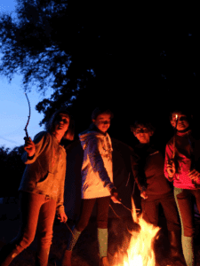 Enfants rassemblés autour d’un feu de camp en soirée pendant un bivouac de stage équestre en Bretagne